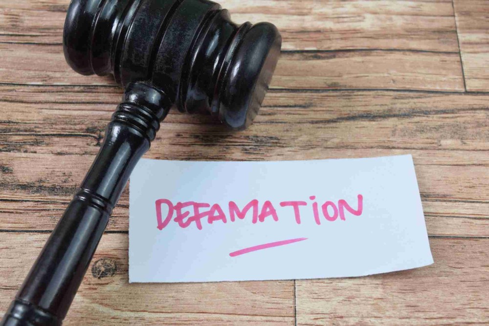 A gavel placed next to a note with the word 'Defamation' written in bold pink letters.