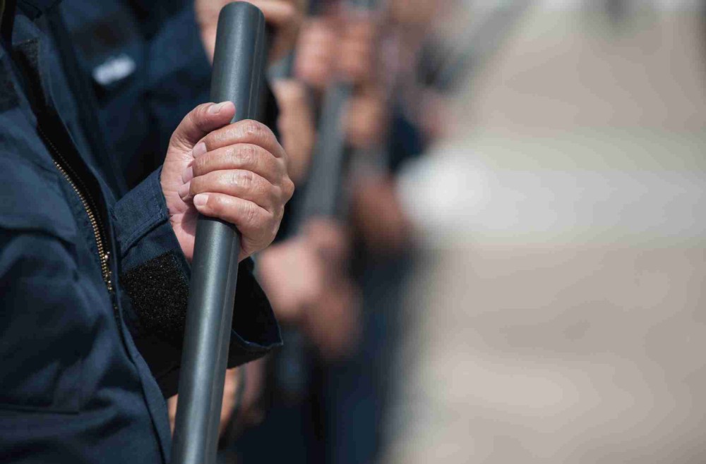 Close-up of a law enforcement officer holding a baton during a lineup.